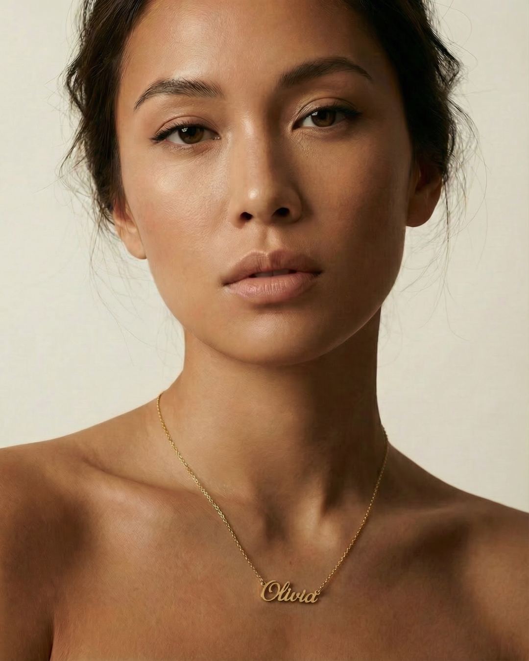 Woman wearing a gold necklace with 'Olivia' engraved on it against a neutral background